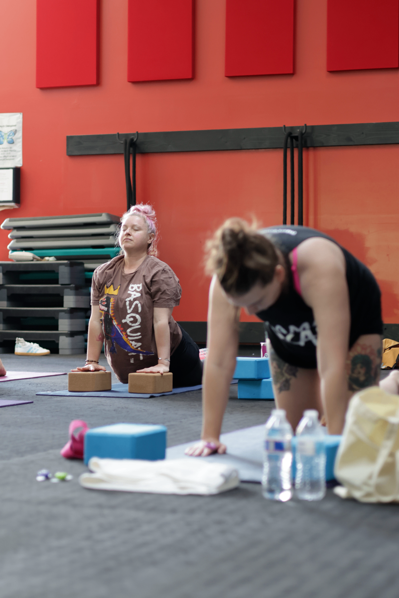 Two women practicing yoga on mats with blocks in a studio with a bright red wall