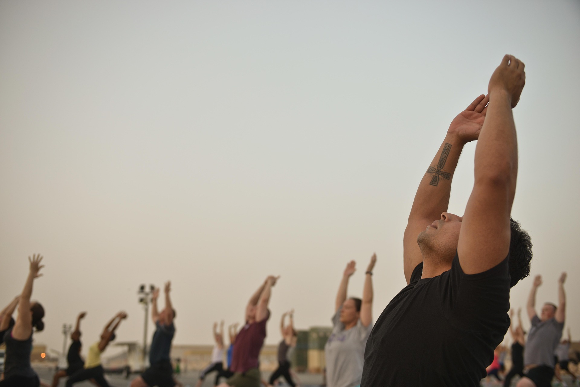 A group of people outdoors reaching their arms overhead in a sun salutation at dusk
